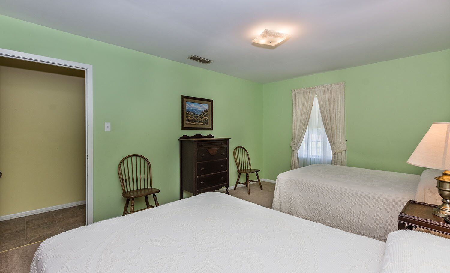 Un dormitorio con dos camas, un aparador, una silla, un cuadro y una ventana con cortinas.