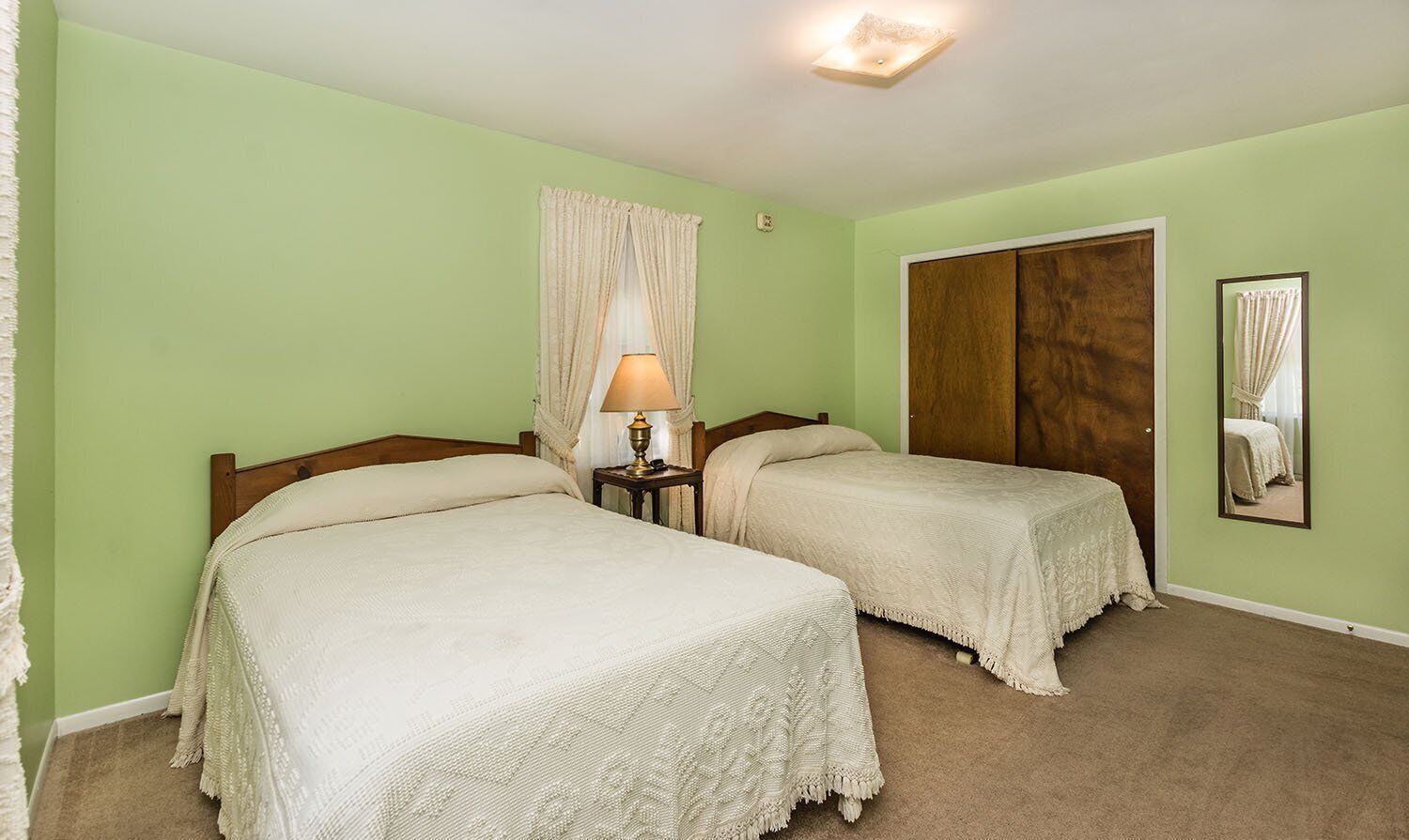 Una habitación con dos camas, una mesita de noche con lámpara, un armario de madera y un espejo en la pared.