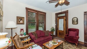 A cozy living room with a wooden ceiling fan, a red armchair, a patterned sofa, and a wooden coffee table.