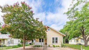 A single-story yellow house with a front porch, surrounded by trees and a well-maintained lawn.