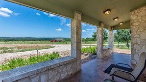 Un espacio al aire libre cubierto con pilares de piedra, vista a un paisaje rural y un edificio rojo en la distancia.