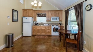 Cocina compacta con armarios de madera, refrigerador, microondas, estufa y una mesa de comedor con sillas.