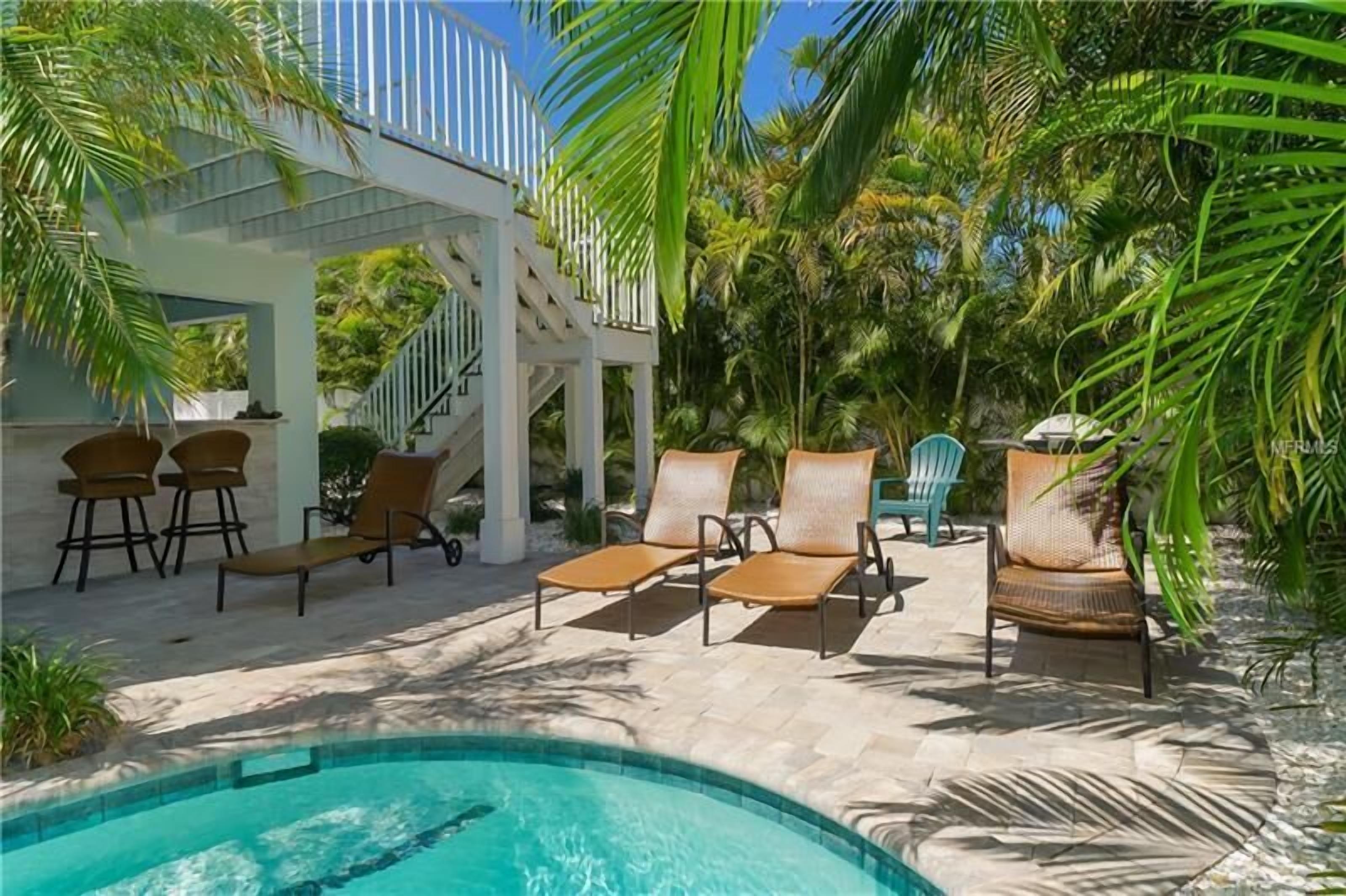 A poolside area with lounge chairs, a covered seating area, and a staircase leading to an upper level.