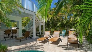 Un espace aménagé au bord de la piscine, avec des chaises longues, un coin salon couvert et un escalier menant à un niveau supérieur.