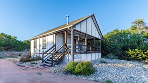 A small, single-story building with a porch and a staircase leading to the entrance, surrounded by gravel and greenery. - Private Hot Tub - Fireplace - 4 min. to downtown - Wildlife (Fredericksburg)