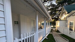 A white porch with a picket fence, a small lawn, and a street view.