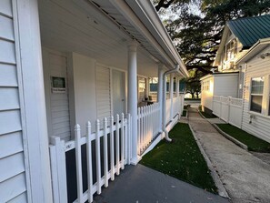 A white porch with a picket fence, a small lawn, and a street view. - Cottage 2 - Porch Bungalow (Fairhope)