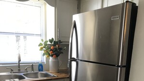 A kitchen with white cabinets, a stainless steel refrigerator, a sink, and a window with blinds.
