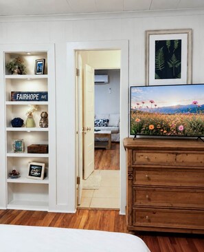 Ein Schlafzimmer mit einem Holzkasten, einem Fernseher, einem Bücherregal und einer Tür zu einem Badezimmer.