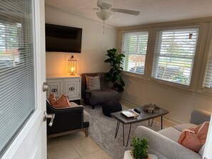 A living room with a sofa, a coffee table, a TV, a plant, and a window with blinds.