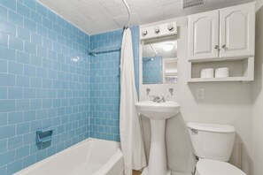 A bathroom with blue tiles, a white bathtub, a white sink, a toilet, and a mirror above the sink.