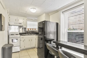 A compact kitchen with white cabinets, a stainless steel stove, a black refrigerator, and a window with blinds.
