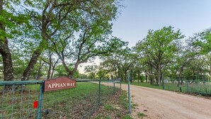 Eine ländliche Straße namens 'Appian Way' mit einem Metallzaun und Bäumen an beiden Seiten.