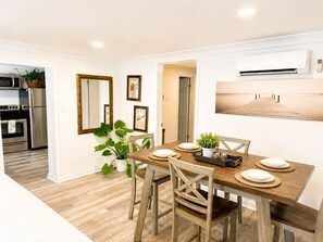 A modern kitchen with stainless steel appliances, a dining area with a wooden table and chairs, and a large mirror on the wall. - Pelicans Perch at The Pelicans House (Fairhope)
