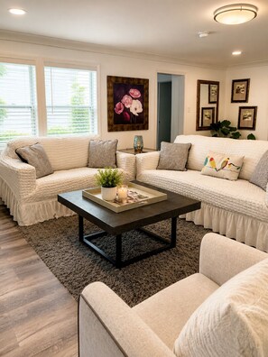 A living room with a sectional sofa, a coffee table, and a painting on the wall. - Pelicans Perch at The Pelicans House (Fairhope)
