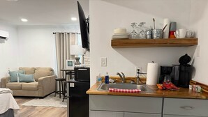 A compact living space with a kitchenette, a sofa, a flat-screen TV, and a dining area with a wooden shelf.