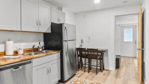 Eine kompakte Küche mit weißen Schränken, einem Edelstahlkühlschrank und einer Holz Arbeitsplatte.