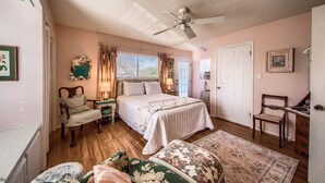 A bedroom with a bed, a chair, a desk, a ceiling fan, and a window with curtains. - harming Downtown Fredericksburg Retreat – Cozy, Walkable, & Vintage (Fredericksburg)