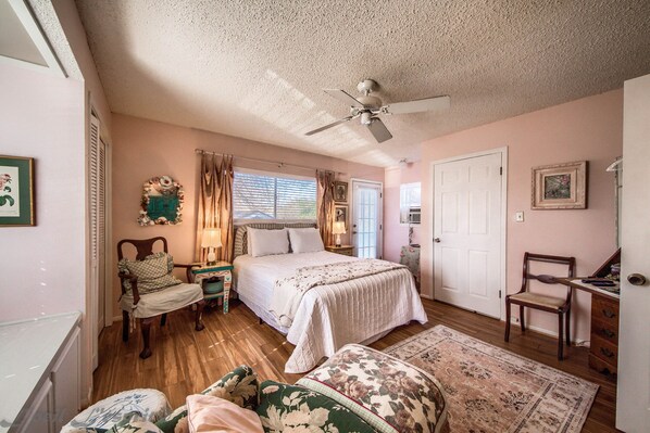 A bedroom with a bed, a chair, a desk, a ceiling fan, and a window with curtains.