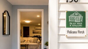 Ein Korridor mit einem Hinweisschild, einem gerahmten Spiegel, einem gemusterten Teppich und einem Schild für 'The Bay House & Bungalows of Fairhope' im Pelicans Perch.