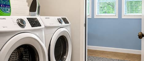 A laundry room with two front-loading washing machines, a green bottle of laundry detergent, and a Samsung iron.