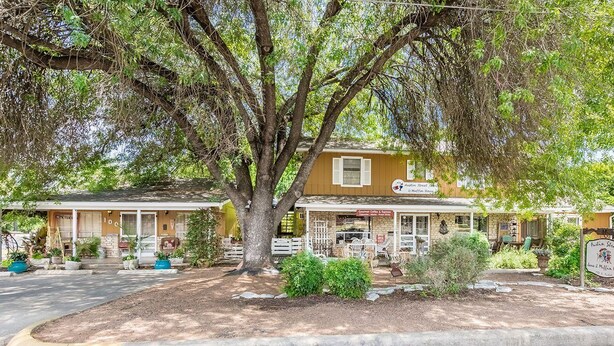 A two-story building with a porch, a sign reading "Austin Street Cafe & Muffin House," and a large tree in front. - Couples Getaway - 1 block to downtown- Jacuzzi tub! (Fredericksburg)
