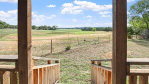 Eine Holzterrasse mit Blick auf ein grasbewachsenes Feld und Bäume unter klarem Himmel.