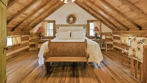 Un dormitorio tipo cabaña de madera con techo de madera, una cama, dos mesitas de noche y una ventana con cortinas.