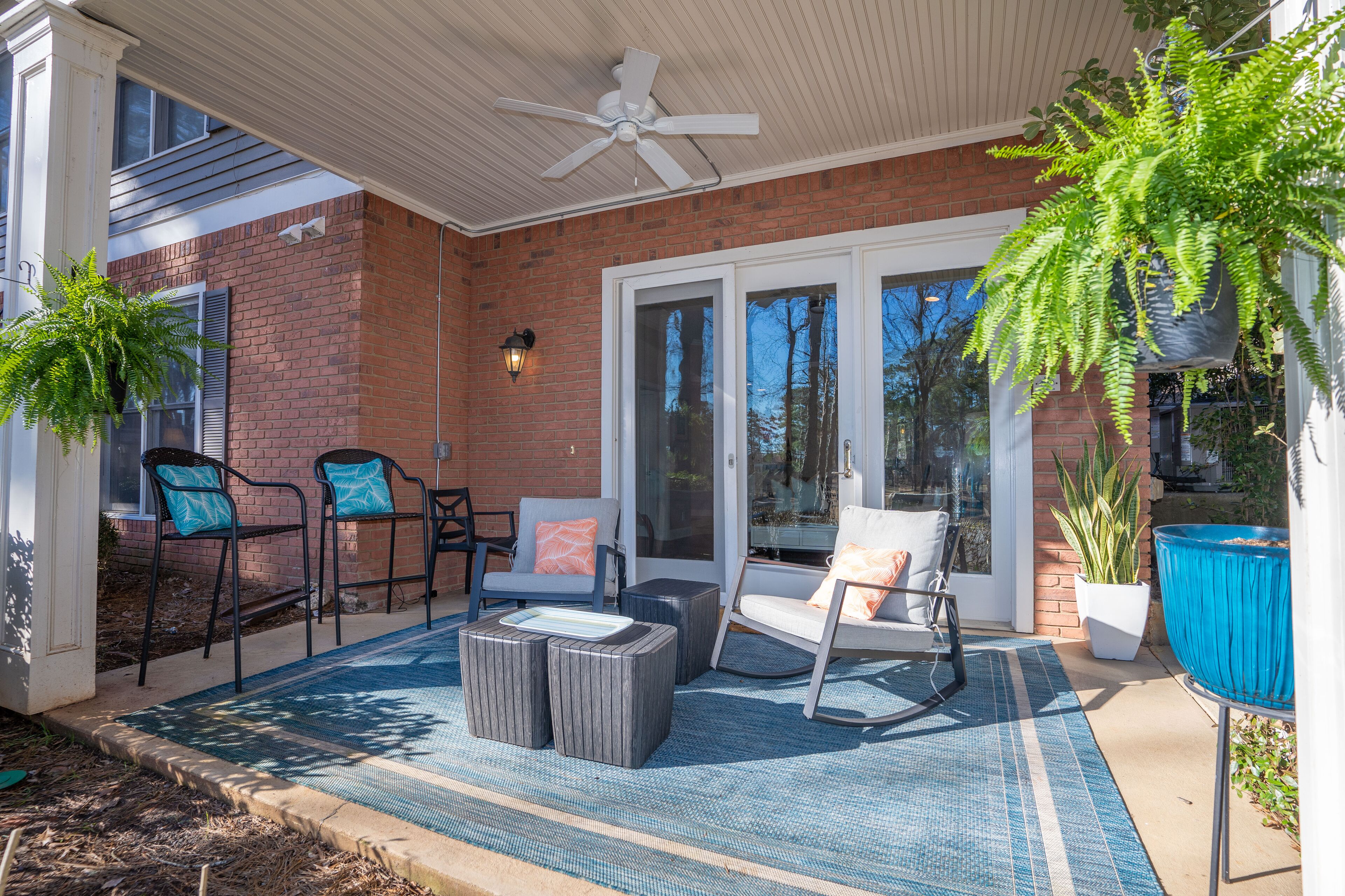 Un patio cubierto con muebles de exterior, ventilador de techo y plantas en macetas.