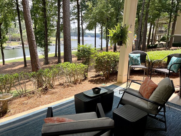 A covered outdoor seating area with a view of a lake, surrounded by trees and shrubs.