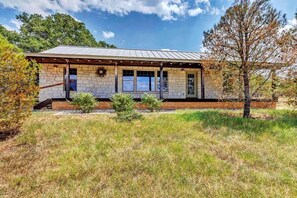 A stone building with a metal roof, a covered porch, and a small garden area. - Private Hot Tub - Newly renovated - Short Drive to downtown (Fredericksburg)