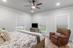 A bedroom with a bed, a TV on a dresser, a brown leather chair, and three windows with blinds. - Private Hot Tub - Newly renovated - Short Drive to downtown (Fredericksburg)