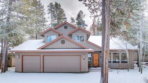 Ein zweistöckiges Haus mit Garage, umgeben von schneebedeckten Bäumen.