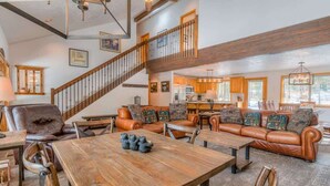 Ein geräumiger Wohnbereich mit einem Holzespeisetisch, Ledersofas und einer Treppe, die in eine obere Ebene führt.