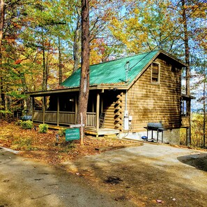 A rustic cabin with a porch, a chimney, and a sign indicating its name and address.