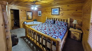 A wooden cabin bedroom with a bed, a ceiling fan, a nightstand, and a window.
