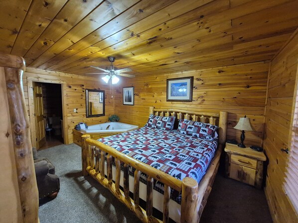 Ein Schlafzimmer einer Holzhütte mit einem Bett, einem Deckenventilator, einem Nachttisch und einem Fenster.