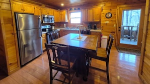 A cabin-style kitchen with wooden walls and floors, stainless steel appliances, and a dining area with a table and chairs.