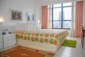 Habitación de hotel con cama, mesita de noche, escritorio y ventana con vista a la ciudad.