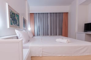 A hotel room with a bed, a television on a stand, and a painting on the wall.