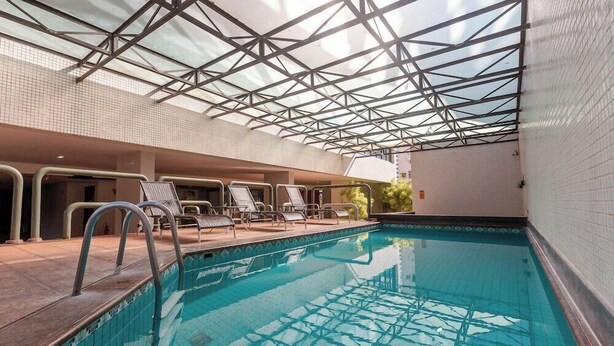 An indoor swimming pool with clear glass ceiling, tiled walls, and lounge chairs along the poolside. - Rede Andrade LG Inn Recife (Recife)