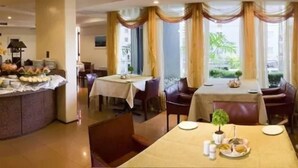 A hotel dining area with tables set for breakfast, a buffet with various food items, and large windows with curtains. - Rede Andrade LG Inn Recife (Recife)