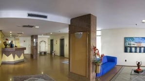 Un vestíbulo amplio con mostrador de recepción, un sofá azul y un jarrón decorativo.