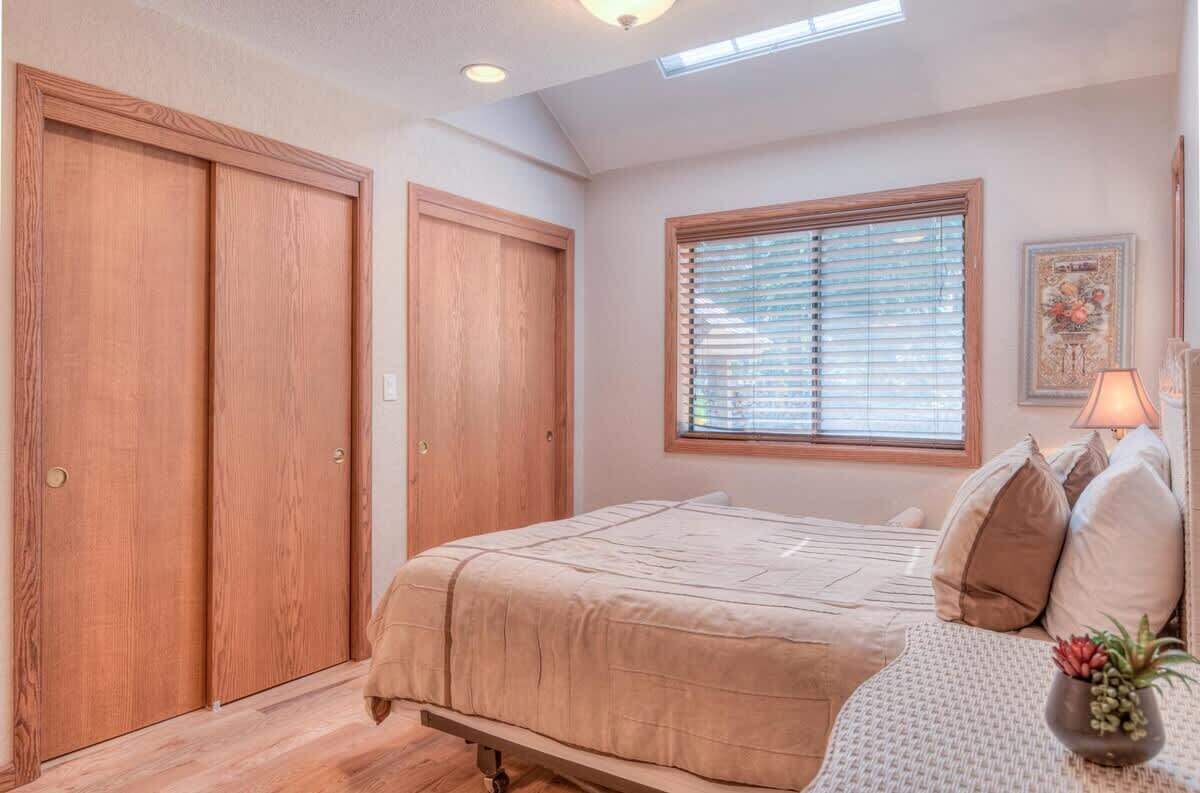 A bedroom with a bed, a window with blinds, a bedside lamp, and a framed picture on the wall.