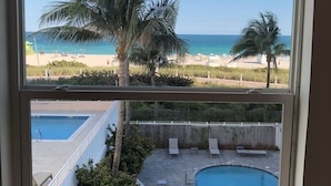 A view of a beach and a swimming pool through a window. - South Beach Ocean View King Bed + Free Beach Service (Miami Beach)