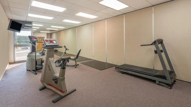 A fitness room with a treadmill, elliptical, and stationary bike, a TV, and a large window. - Budget Inn Laramie (Laramie)