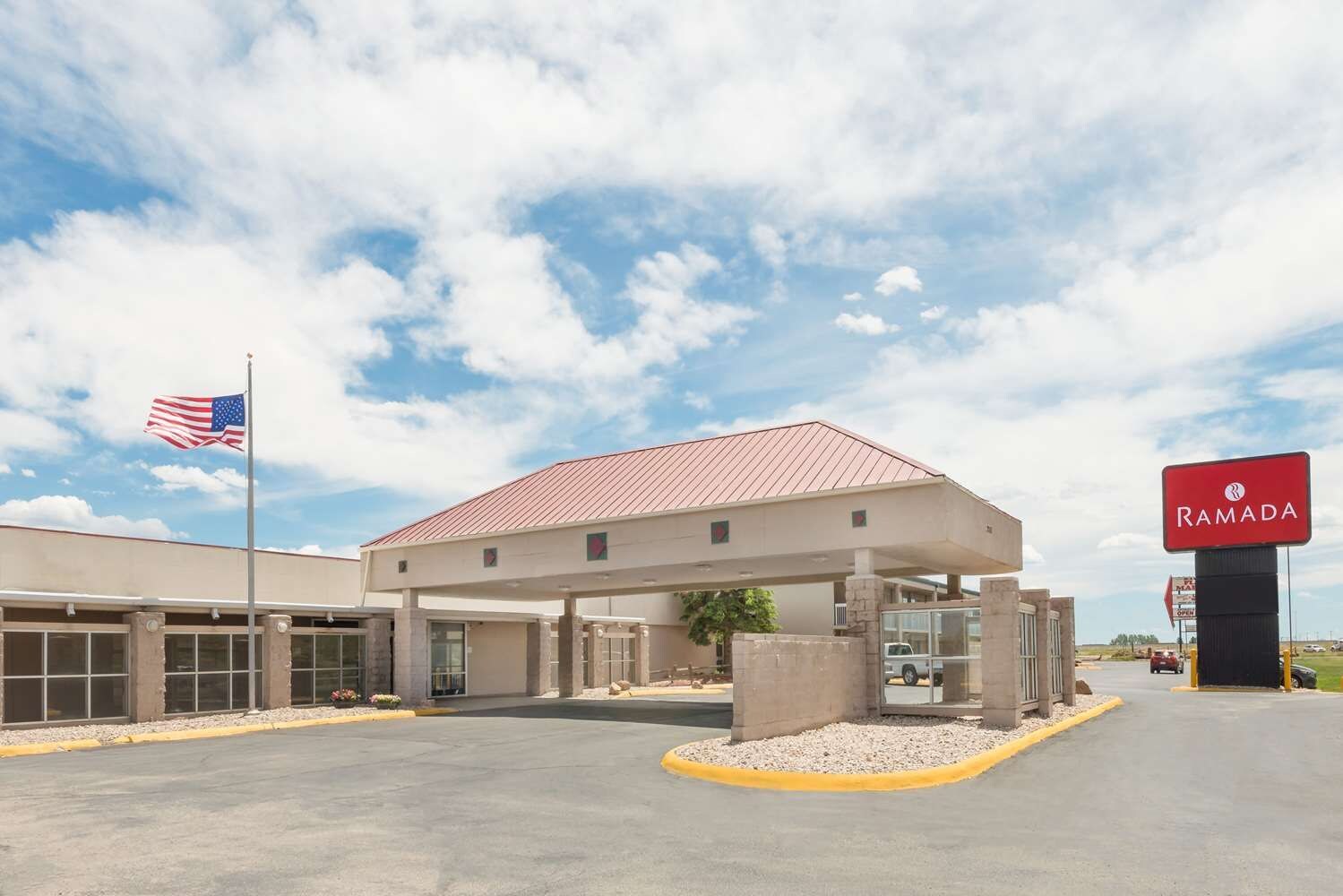 A Ramada hotel with a covered parking area, a flag, and a clear sky.