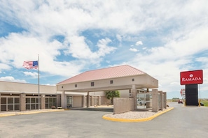 A Ramada hotel with a covered parking area, a flag, and a clear sky. - Budget Inn Laramie (Laramie)