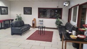 A modern office space with two leather sofas, a small table with bowls, a red rug, and framed pictures on the walls. - Budget Inn Laramie (Laramie)