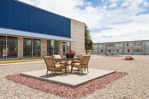 An outdoor seating area with a table and chairs, surrounded by a gravel and pebble ground, in front of a building with large windows and a blue exterior wall. - Budget Inn Laramie (Laramie)